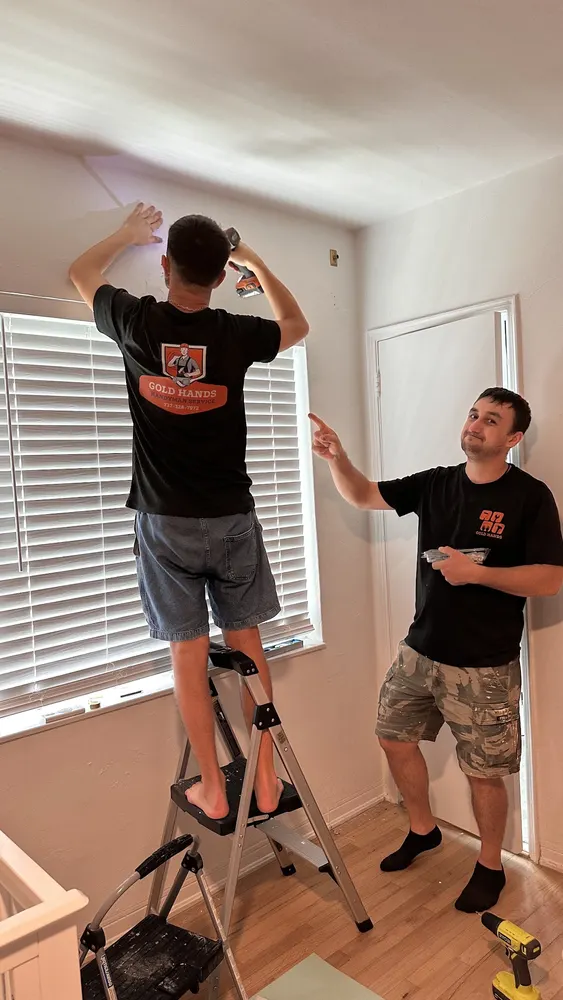 Two Gold Hands technicians installing a fixture in a bedroom